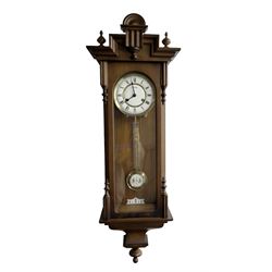 German - 20th century 8-day spring driven wall clock in a 19th century styled mahogany case, case with a carved pediment, finials and ogee base, fully glazed door with a two part enamel dial, Roman numerals and gridiron pendulum, Hermle twin train striking movement, sounding the hours and half hours on a gong. With key.