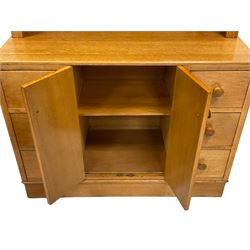 E Gomme - Vintage light oak dresser, the arch top with two glazed doors opening to reveal one fixed shelf over two cupboard doors flanked by six drawers, raised on a plinth base 