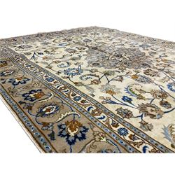 Persian Kashan ivory ground rug, the field with a central floral medallion surrounded by scrolling tendrils of branches with palmette motifs, the multi-band border with repeating stylised floral patterns and acanthus leaves