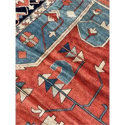 Large Persian Heriz carpet, red ground with geometric star medallion, surrounded by angular vine and geometric motifs, blue ground guarded border band decorated with a series of stylised flower heads and trailing foliate