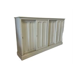 Painted side cabinet, the projecting rectangular top over four sliding doors, opening to reveal two fixed shelves, raised on a plinth base