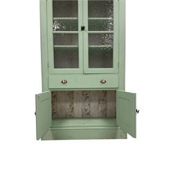 Kitchen cupboard painted mint green, the projecting top over two glazed cupboard doors, opening to reveal two fixed shelves over one drawer and two cupboard doors, raised on a plinth base 