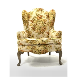 20th century wing back armchair, upholstered in floral fabric with squab cushion, raised on cabriole front supports 