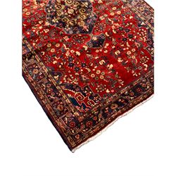 Persian crimson ground rug, the indigo floral pole medallion within a busy field of swirling branches with flower heads and stylised plant motifs, the multi-band border with geometric floral symbols 