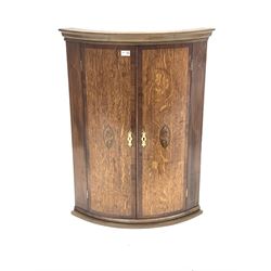 Early 20th century oak and mahogany banded bow front corner cupboard, the two doors each inlaid with shell motif enclosing two shelves, W70cm, H93cm, D48cm