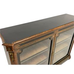 Victorian ebonised and amboyna wood credenza pier cabinet, rectangular moulded top with extending canted corners, mounted throughout with gilt metal beading, the frieze with ebonised panels and central inlaid scrolling and interlaced cartouche, enclosed by two glazed doors with inlaid upper spandrels, the canted uprights mounted with gilt metal lion masks on torches with foliate swags over matching inlays and lower acanthus leaf mount, the skirted base with foliate moulded band and ebonised inlaid panels, on turned feet