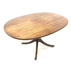 Georgian mahogany breakfast table, oval tilt top on turned pedestal base, four out splayed supports with brass cups and castors, 133cm x 96cm, H72cm