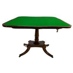 Early 19th century mahogany card table, rectangular fold-over and swivel top with rounded front corners, turned pedestal with plinth base and four splayed sabre supports with carved reeding, on brass castors