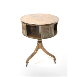 20th century Regency design mahogany drum table, the circular revolving top having faux books and recesses for further books, raised on turned column and three inverted splayed supports terminating in brass castors