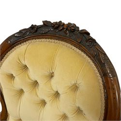 Victorian walnut open armchair, the arched cresting rail carved with flower heads with extending foliage, upholstered in pale yellow buttoned fabric, scroll carved arm terminals over serpentine supports and cabriole feet, carved with flower heads, foliage and berries, shaped lower rail carved with further decoration, the feet terminals carved with scrolled leaves, on brass castors 