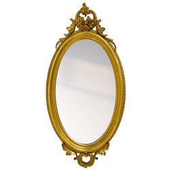 19th century giltwood and gesso wall mirror, moulded oval frame with scrolled cartouche pediment decorated with flower heads and trailing foliage, the outer frame with shell moulding, C-scroll and foliage lower decoration 