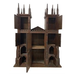 Large late 19th to early 20th century oak cabinet in the form of the York Minster western front, depicting the two towers with crocketed pinnacles over carved tracery work windows, fitted with a combination of compartments enclosed by small doors disguised as windows, central portal door and flanking side doors, sloped arched pediment inscribed 'West front of York Minster as seen from the ancient ramparts', decorated with pointed niches with carved figures 