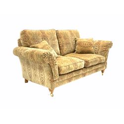 Parker Knoll - two seat sofa, upholstered in golden medallion fabric, with two small cushions and supported by two brass castors. W 180cm, height to seat 49cm. 