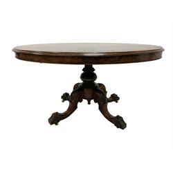 Mid-to late century walnut loo table, oval top with moulded edge and quarter match finish, fluted and turned pedestal with foliate carving over swept cabriole supports with scrolling and flower head decoration on ceramic castors 