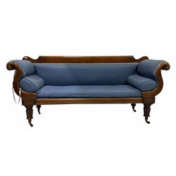 William IV mahogany scroll settee, the plain cresting rail over scroll shaped arm supports, raised on lobe carved front supports terminating at brass cups and castors, upholstered in blue fabric with squab and baluster cushions
