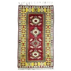 Turkish crimson ground rug, the field with four central lozenges with foliate and flower head decoration, the guarded border with wide yellow band decorated with repeating geometric motifs, outer ivory guard with flower heads