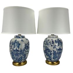 Pair of blue and white table lamps, each of ginger jar form, painted with a continuous landscape, raised upon circular gilt bases, H35cm 