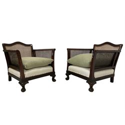 Pair of early to mid-20th century walnut framed bergere armchairs, serpentine cresting rail with canework back and arms, the scrolled arm terminals carved with acanthus leaves, sprung seat over moulded frieze decorated with Greek key design, raised on ogee cabriole supports with ball and claw feet, with loose cushions