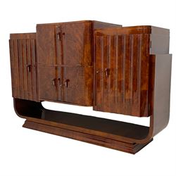 Attributed to Harry & Lou Epstein - Art Deco circa. 1930s figured walnut sideboard, central fall-front cocktail cabinet with raised top enclosing mirrored interior with bottle insets, over double cupboard, flanked by scalloped fluted doors concealing shelves and rotating bottle stand, curved supports on undertier with moulded base