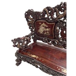 Early 20th century Chinese hardwood settee or hall-bench, the back pierced and heavily carved with dragons and trailing flower heads, the seat backs with mother of pearl inlays depicting warriors on horse-back and traditional landscapes, the arms carved as a dragon with agape mouth and mother of pearl inlaid scales, scaled fish feet terminating to masks