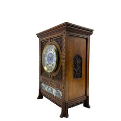 Carved oak cased 8-day striking and chiming mantle clock in the style of William Morris c1880, rectangular case raised on four pilasters with outwardly projecting carved feet, with a two-fold moulded pediment and flat top, incised carving to the front and carved floral leafed spandrels to the dial, below a recessed blue and white porcelain panel depicting flowers and leaves, side panels with a carved leaf motif and rear case door with scroll fretwork, circular blue and white porcelain dial with floral decoration, white roundels with blue Arabic numerals and blue steel fleur di Lis hands, German or possibly English three-train eight-day rack striking movement, striking the hours on a coiled gong and the quarters on a nest of eight underslung bells. With pendulum & Key.



