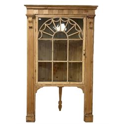 Early 20th century pine corner cabinet, the projecting cornice over a fluted frieze, fitted with astragal glazed door with swag decoration enclosing two shelves, the door flanked by fluted column uprights, the rear support terminating in spade foot 