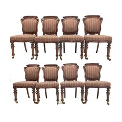 Set eight Victorian mahogany dining chairs, cartouche shaped backs with applied carved floral roundels, upholstered in striped fabric, raised on turned front supports with brass cup and ceramic castors