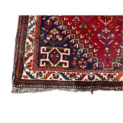 Persian Shiraz red ground rug, the central geometric medallion lozenge and matching spandrels decorated with central Koçboynuzu motifs, the field with all-over stylised plant symbols, guarded ivory border with repeating foliate patterns