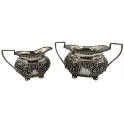 Late Victorian silver three piece tea set embossed with panels of flower heads and scrolls on ball feet, the teapot with ebonised handle and lift Birmingham 1898 Maker Joseph Gloster