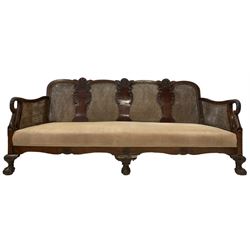 Early 20th century walnut bergère two seat sofa, the back and arms with double cane panels, the shaped back carved and applied with foliate and shell decoration and stylised palms, upholstered in latte corduroy fabric with sprung seat and loose cushions, raised on cabriole supports with ball and claw feet 