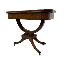 Regency mahogany tea table, rectangular fold-over and swivel top, raised on curved support with beaded collar and concave quadruform base decorated with applied roundells, on four sabre supports with brass paw feet and castors