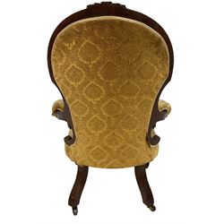 Victorian mahogany framed armchair, cresting rail carved with scrolling foliate cartouche over rolled arms, back and sprung seat upholstered in buttoned floral patterned mustard fabric, on turned and fluted supports with castors