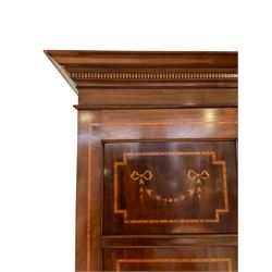 Edwardian inlaid mahogany triple wardrobe, projecting cornice above frieze inlaid with chequered banding, the central door with bevelled mirror plate and two flanking panelled doors decorated with ribbon and garland inlay, interior fitted with hanging rail, three open drawers over three graduating drawers, on plinth base
