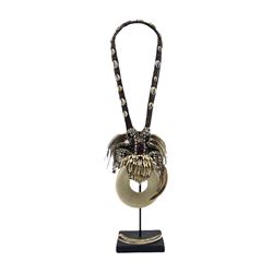 Papua New Guinea Pectoral or necklace, woven fibre and shell strap, inset with wild boar teeth, two tusks (one loose), feathers and carved shell pendant, on stand H63cm