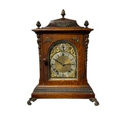 Winterhalder & Hoffmeier  - 8-day quarter-striking German mantle clock in an oak case c1900, curve topped pediment with pineapple finials, glazed arched door on a broad plinth raised  on scroll feet, brass dial with a matted dial centre and silvered chapter ring with Roman numerals and fleur di Lis hands, pendulum regulation dial to the arch, two-train ting-tang movement sounding the quarters and hours on two coiled gongs. With pendulum & key.