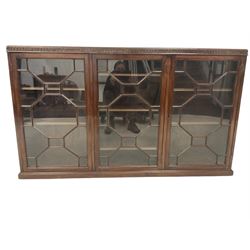 Early 20th century Georgian design enclosed bookcase, the blind-fretwork frieze in the form of repeating Vitruvian waves, fitted with three astragal glazed doors, each enclosing three adjustable shelves, on plinth  base