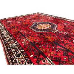 Persian crimson ground rug, the field decorated with a central indigo hexagonal medallion, surrounded by columns of stylised geometric tree motifs, the guarded ivory border with repeating patterns