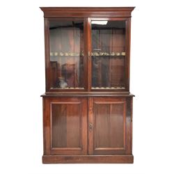Mahogany gun cabinet , the projecting cornice over two glazed doors, opening to reveal fifteen gun holders, over two cupboard doors with two shelves, raised on a plinth base 