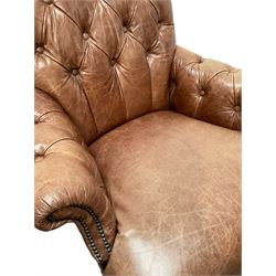 Tetrad - tub shaped armchair upholstered in buttoned tan leather, rolled back and arms, with stud work, raised on turned supports 