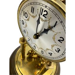 A 20th century German torsion pendulum clock with a 3-3/4” silvered dial, Arabic numerals, minute track and garland swags, steel spade hands, 400-day spring driven movement with a four-ball rotary pendulum and pendulum lock, clear glass dome on circular brass effect base with adjustable feet.
