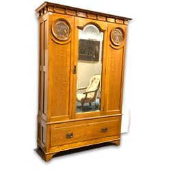 Early 20th century oak wardrobe, the projecting cornice over frieze with applied corbels, single arched bevel edge mirrored door enclosing interior fitted for hanging, flanked by panels carved with acanthus leaves, drawer to base, raised on stile supports W133cm H197cm, D48cm