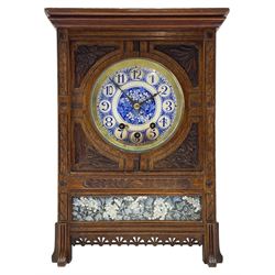 Carved oak cased 8-day striking and chiming mantle clock in the style of William Morris c1880, rectangular case raised on four pilasters with outwardly projecting carved feet, with a two-fold moulded pediment and flat top, incised carving to the front and carved floral leafed spandrels to the dial, below a recessed blue and white porcelain panel depicting flowers and leaves, side panels with a carved leaf motif and rear case door with scroll fretwork, circular blue and white porcelain dial with floral decoration, white roundels with blue Arabic numerals and blue steel fleur di Lis hands, German or possibly English three-train eight-day rack striking movement, striking the hours on a coiled gong and the quarters on a nest of eight underslung bells. With pendulum & Key.



