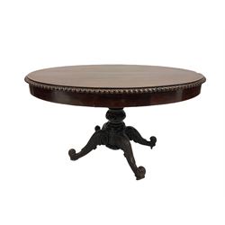 Early 19th century rosewood pedestal table, the oval top with carved moulded edge over two frieze drawers, raised on a turned column leading into four splayed and scrolled supports, terminating in wooden castors W135cm, H75cm, D95cm 