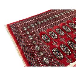 Persian Tekke Bokhara crimson ground rug, the field decorated with three rows of repeating Gul motifs, the multi-band border with stylised plant motifs in contrasting colours and geometric designs