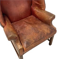 Georgian design mahogany framed wingback armchair, high back shaped cresting rail over down-scrolled arms, upholstered in tan leather with studwork border and loose seat cushion, raised on moulded square supports united by H-stretcher