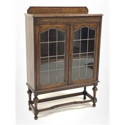 Early 20th century oak display cabinet, carved frieze over two lead glazed doors, turned supports connected by stretchers, W92cm, H134cm, D32cm