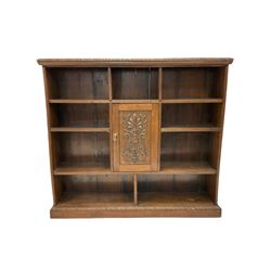 Open oak bookcase, the carved and moulded edge over seven shelves with one central carved cupboard, raised on a plinth base W165cm, H145cm, D38cm 