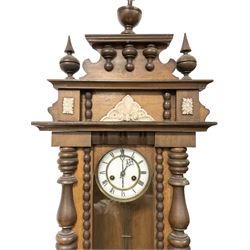 German - mid 19th century spring driven 8-day wall clock in an oak and mahogany case, with a turned and carved pediment, full length glazed case door flanked by ring turned columns and an ogee plinth with pendants, two part enamel dial with pierced steel hands, Roman numerals and minute track,  with a visible gridiron pendulum and striking movement, sounding the hours on a coiled gong.