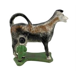 Early 19th century creamware cow creamer, probably Yorkshire, with curled tail handle, a milkmaid seated to one side with pail, decorated with sponged black and ochre and set concave base, painted in green, L17cm x H15cm