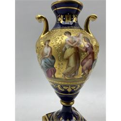 Pair of 'Vienna' porcelain urns, of typical urn form with gilt scroll handles, cobalt blue ground and gilt bands painted with continuous scenes of 'Paris and Helena' & 'Diana im Bade', the other painted with similar scenes, titled beneath, raised on square bases, beehive mark in blue, H23cm